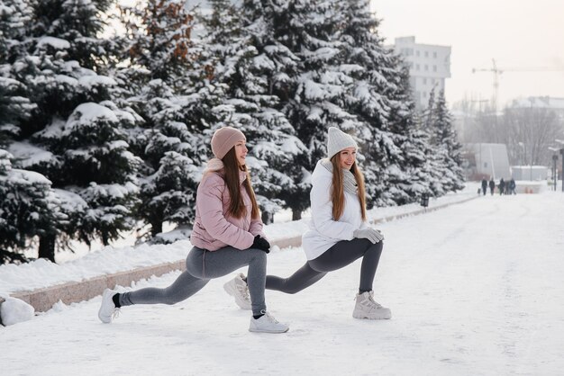 Dos jóvenes atléticas hacen un calentamiento antes de correr en un soleado día de invierno. Una forma de vida sana.