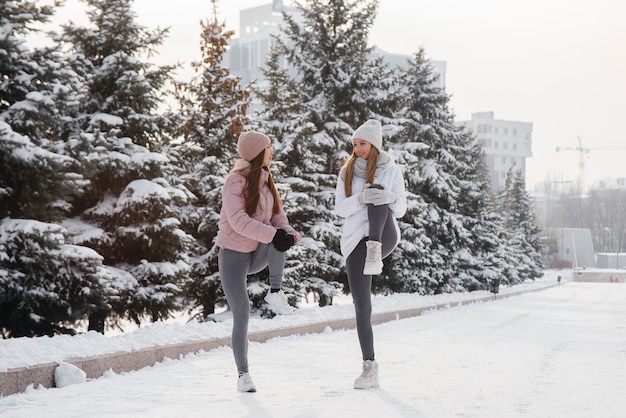 Dos jóvenes atléticas hacen un calentamiento antes de correr en un soleado día de invierno. Una forma de vida sana.