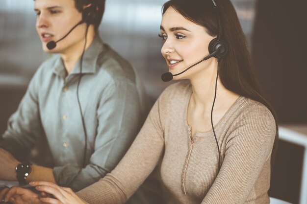 Dos jóvenes con auriculares hablan con los clientes mientras están sentados en el escritorio de una oficina. Centrarse en la mujer. Operadores de call center en el trabajo.