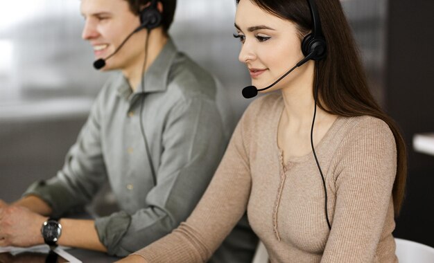 Dos jóvenes con auriculares hablan con los clientes mientras están sentados en el escritorio de una oficina. Centrarse en la mujer. Operadores de call center en el trabajo.