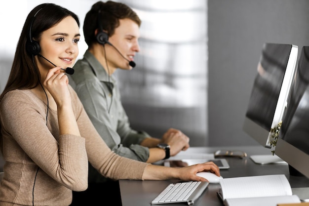 Dos jóvenes con auriculares hablan con los clientes mientras están sentados en el escritorio de una oficina Centrarse en la mujer Operadores del centro de llamadas en el trabajo