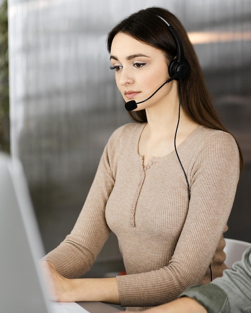 Dos jóvenes con auriculares hablan con los clientes mientras están sentados en el escritorio de una oficina moderna. Centrarse en la mujer. Operadores de call center en el trabajo.