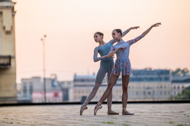 Dos jóvenes bailarinas bailando en zapatos de punta en la ciudad con el telón de fondo del cielo del atardecer