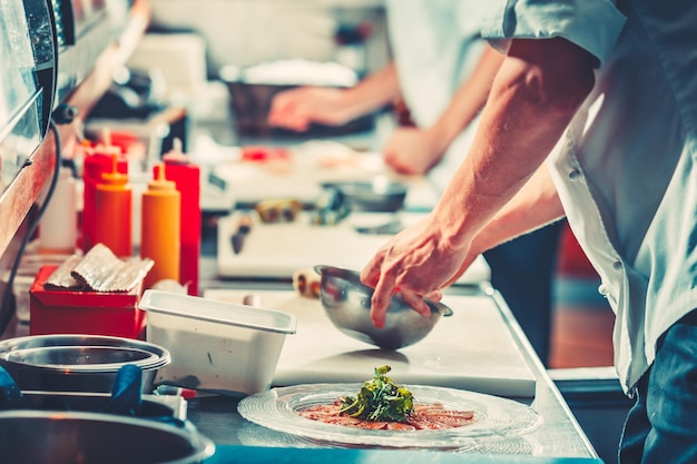 Dos jóvenes chefs en uniforme blanco preparando una deliciosa ensalada de bocadillos de carne de pescado solo con las manos cerca