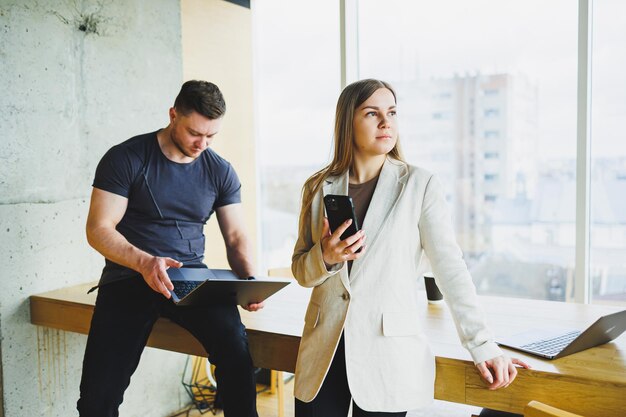 Dos jóvenes colegas, un hombre y una mujer, trabajando juntos en un espacio de trabajo moderno Dos jóvenes empresarios sonriendo alegremente mientras trabajan con una computadora portátil Los colegas se sientan juntos en la mesa