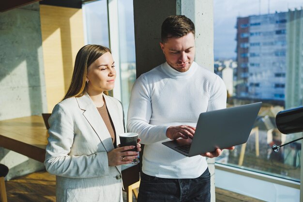 Dos jóvenes colegas prometedores, un hombre y una mujer, están hablando y trabajando en un nuevo proyecto en una computadora portátil Trabajar en una oficina moderna y luminosa Trabajo en equipo