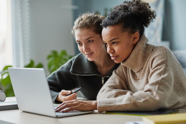 Dos jóvenes colegas sentados en la mesa frente a la computadora portátil y mirando la pantalla durante la videollamada