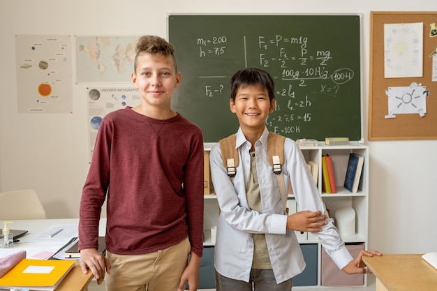 Dos jóvenes colegiales de diversas etnias de pie junto a la pizarra