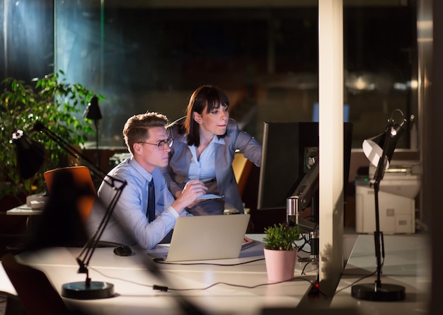 Dos jóvenes diseñadores están trabajando en un nuevo proyecto en la oficina nocturna utilizando tecnología moderna.