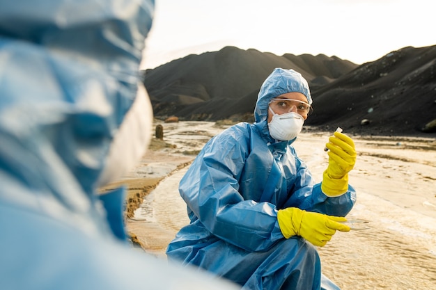 Una de las dos jóvenes ecologistas con guantes de goma, overoles protectores, anteojos y respiradores sosteniendo una muestra de agua tóxica