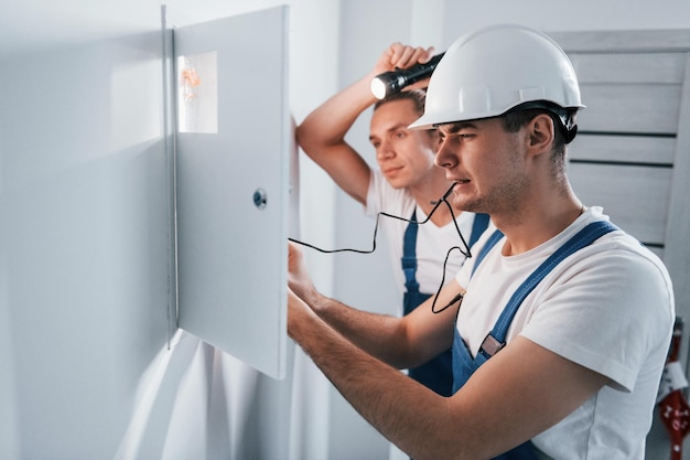 Dos jóvenes electricistas trabajan juntos en interiores usando una linterna