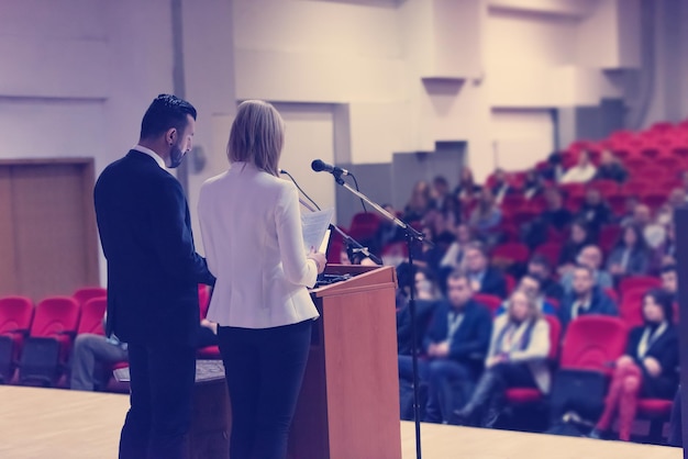 dos jóvenes empresarios dando una presentación a un grupo de colegas sentados en sillas en la sala de conferencias