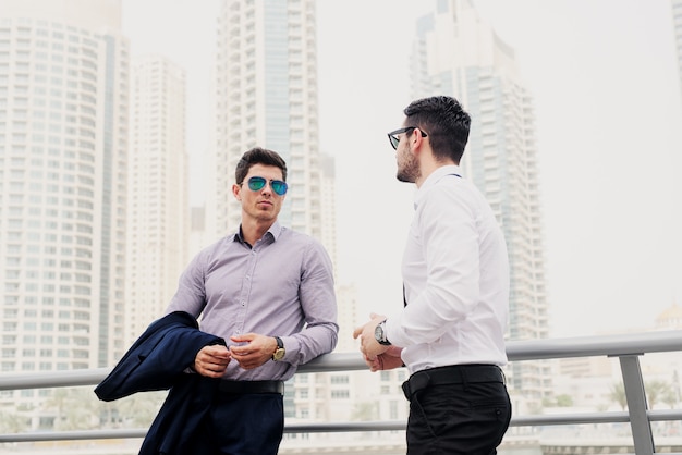 Dos jóvenes empresarios modernos en Dubai Marine se apoyaron en la valla. De pie y discutiendo sobre negocios.