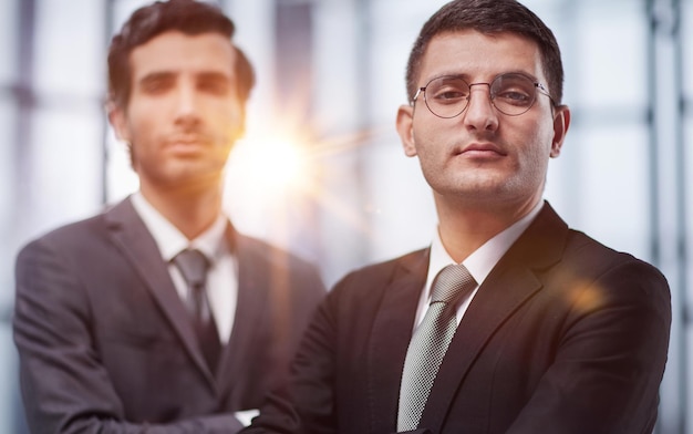 Foto dos jóvenes empresarios serios de pie con los brazos cruzados en la oficina