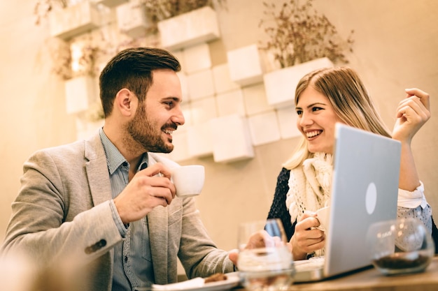 Dos jóvenes empresarios sonrientes hablando y trabajando en una laptop en un descanso en el café.