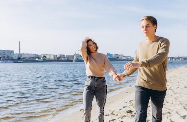 Dos jóvenes enamorados corriendo en la playa Se sonríen el uno al otro Hermosa pareja Sensación de playa Vístete con un suéter