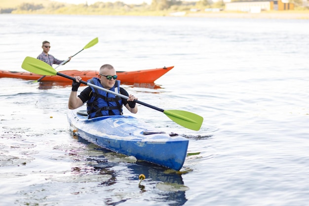 Dos jóvenes están sentados en kayaks y remando en el lago El concepto de entretenimiento acuático