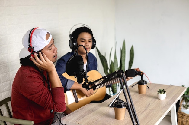 Dos jóvenes de estilo informal grabando música en un estudio de podcast, cantando y tocando la guitarra.