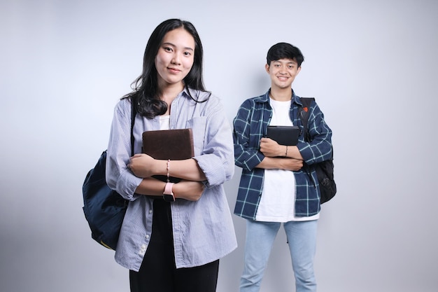 Dos jóvenes estudiantes asiáticos felices amigos de pie con confianza con los brazos cruzados mientras sostienen un libro