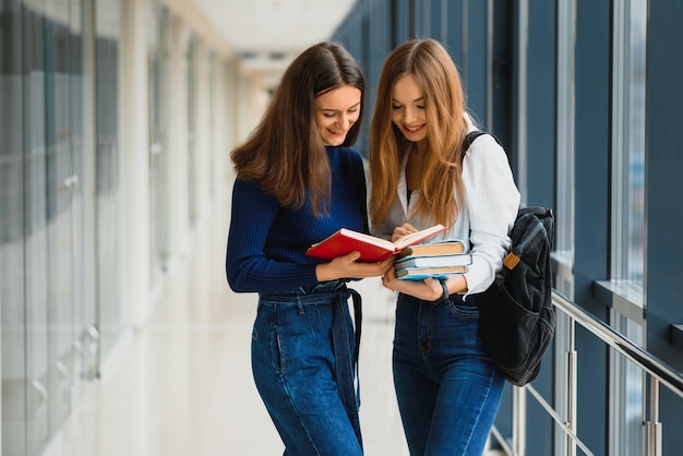Dos jóvenes estudiantes de pie con libros y bolsas en el pasillo