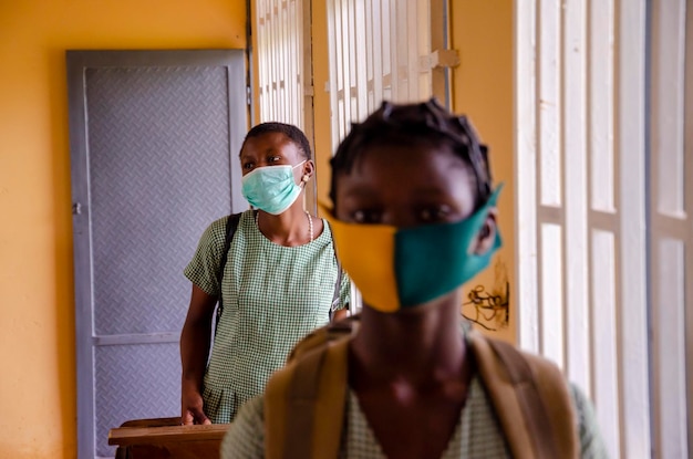 Dos jóvenes estudiantes de primaria con mascarilla mientras previenen, previenen, previenen a sí mismos mientras observan el distanciamiento social en el aula