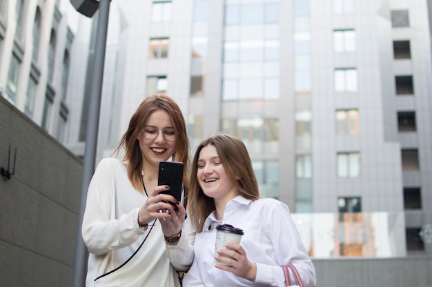 Dos jóvenes estudiantes en el recreo mirando el teléfono inteligente se comunican y sonríen sinceramente