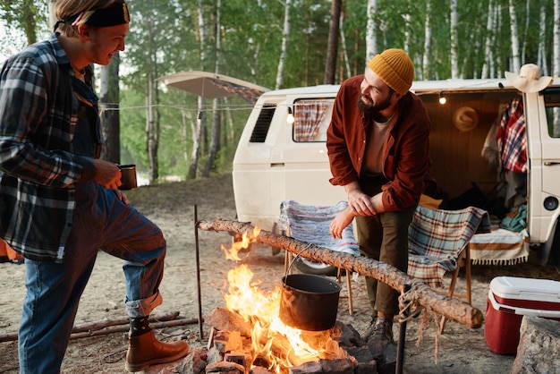 Dos jóvenes excursionistas cocinando comida juntos en una fogata en el bosque