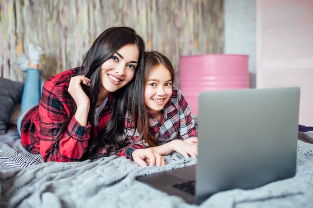 Foto dos jóvenes hermanas de adolescentes usando laptop para buscar reuniones de películas en casa en la habitación de la cama. posando para la camara