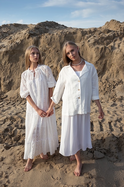 Dos jóvenes hermanas gemelas posando en el desierto o cantera de arena en elegante ropa blanca