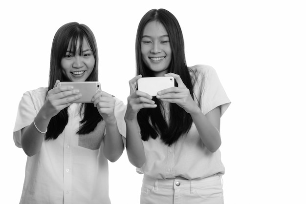 Dos jóvenes hermosas adolescentes asiáticas juntos aislados contra la pared blanca en blanco y negro