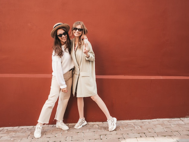 Dos jóvenes hermosas chicas hipster sonrientes en abrigo y suéter blanco de moda