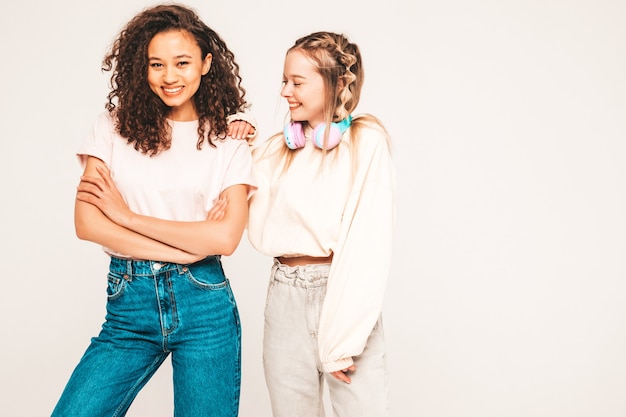 Dos jóvenes hermosas mujeres hipster internacional sonriente en ropa de moda de verano. mujeres despreocupadas, posar, en, estudio