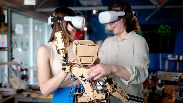 Dos jóvenes ingenieros arreglando un robot mecánico en el taller usando auriculares de realidad virtual VR