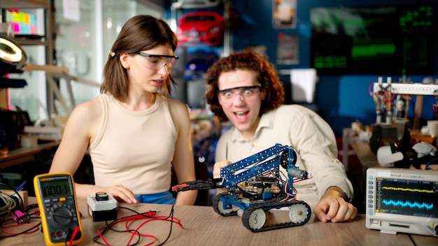 Dos jóvenes ingenieros felices arreglando un automóvil robot mecánico en el taller usando realidad virtual VR