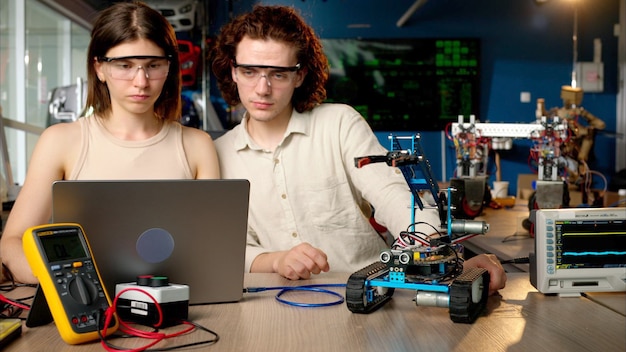 Dos jóvenes ingenieros felices arreglando un automóvil robot mecánico en el taller usando realidad virtual VR