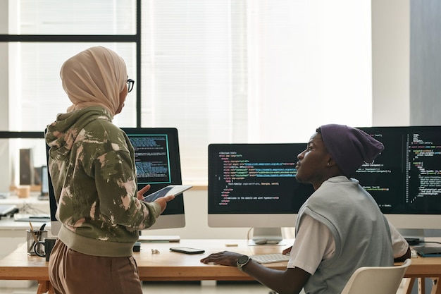 Dos jóvenes ingenieros informáticos interculturales discutiendo formas de descifrar datos