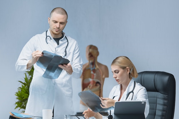 Dos jóvenes médicos especialistas están discutiendo cuidadosamente una radiografía en una oficina luminosa.