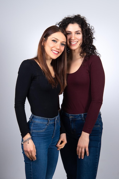 Foto dos jóvenes modelos femeninos sonrientes en jeans parados uno al lado del otro y mirando a la cámara