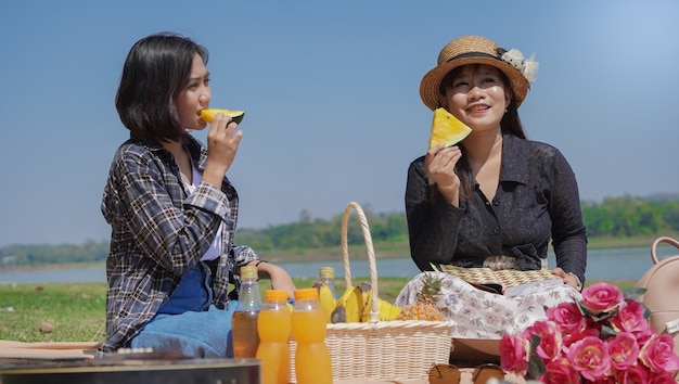 Dos jóvenes mujeres asiáticas comiendo sandía durante sus vacaciones en el lago