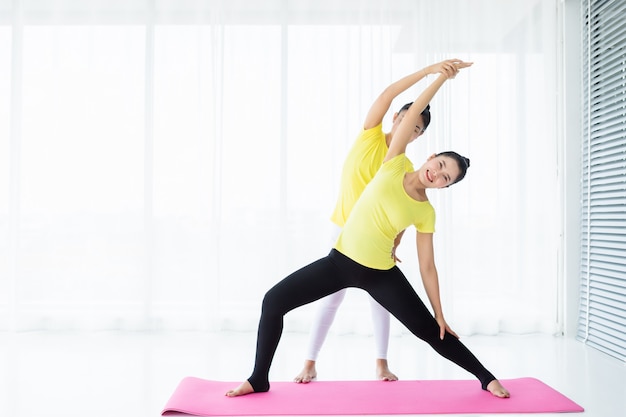 Dos jóvenes mujeres asiáticas entrenan practicando yoga en vestido amarillo o posan con un entrenador y practican