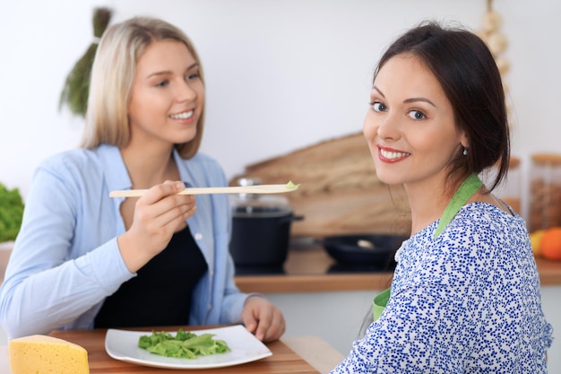 Dos jóvenes mujeres felices están cocinando en la cocina Los amigos se divierten mientras preparan una comida saludable y sabrosa