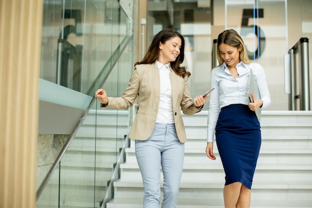 Dos jóvenes mujeres de negocios caminando por las escaleras en el pasillo de la oficina