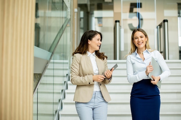 Dos jóvenes mujeres de negocios caminando por las escaleras en el pasillo de la oficina