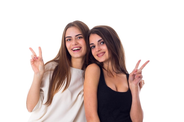 Foto dos jóvenes mujeres sonrientes con camisas blancas y negras que muestran paz sobre fondo blanco en el estudio