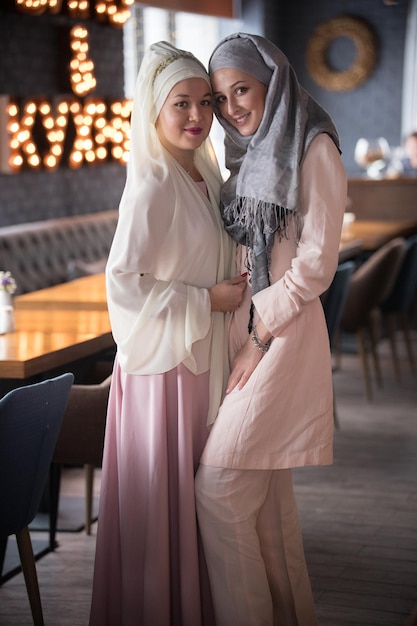 Dos jóvenes musulmanas sonrientes con bufanda en la cabeza de pie en el café