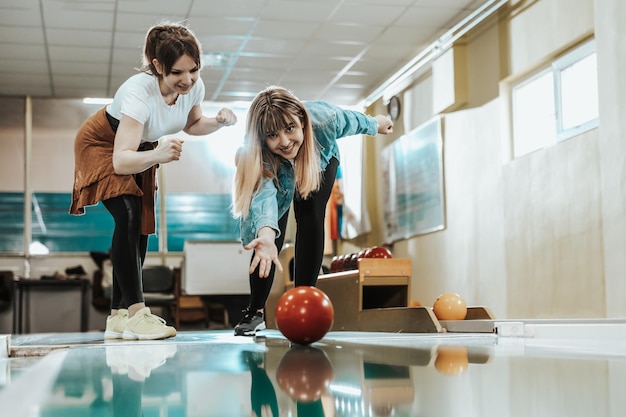 Dos jóvenes sonrientes divirtiéndose mientras lanzan la bola de bolos y aceleran el tiempo juntos.