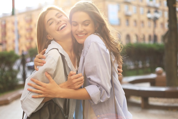 Dos jóvenes sonrientes mujeres hipster en ropa de verano posando en la calle. Mujer mostrando emociones positivas en la cara.
