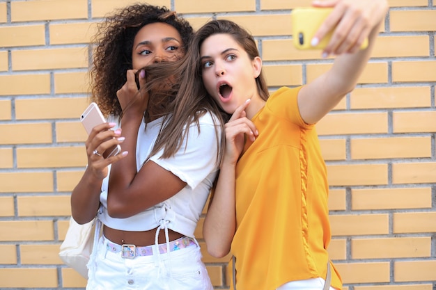 Dos jóvenes sonrientes mujeres hipster en ropa de verano posando en la calle. Mujer mostrando emociones positivas en la cara.