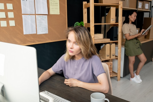 Dos jóvenes trabajadoras contemporáneas de la sala de almacenamiento que controlan y reciben pedidos en línea de los clientes mientras usan la computadora y el panel táctil