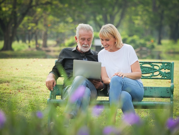 Dos jubilaciones de personas mayores felices El hombre y la mujer están sentados y usando una computadora portátil en el parque
